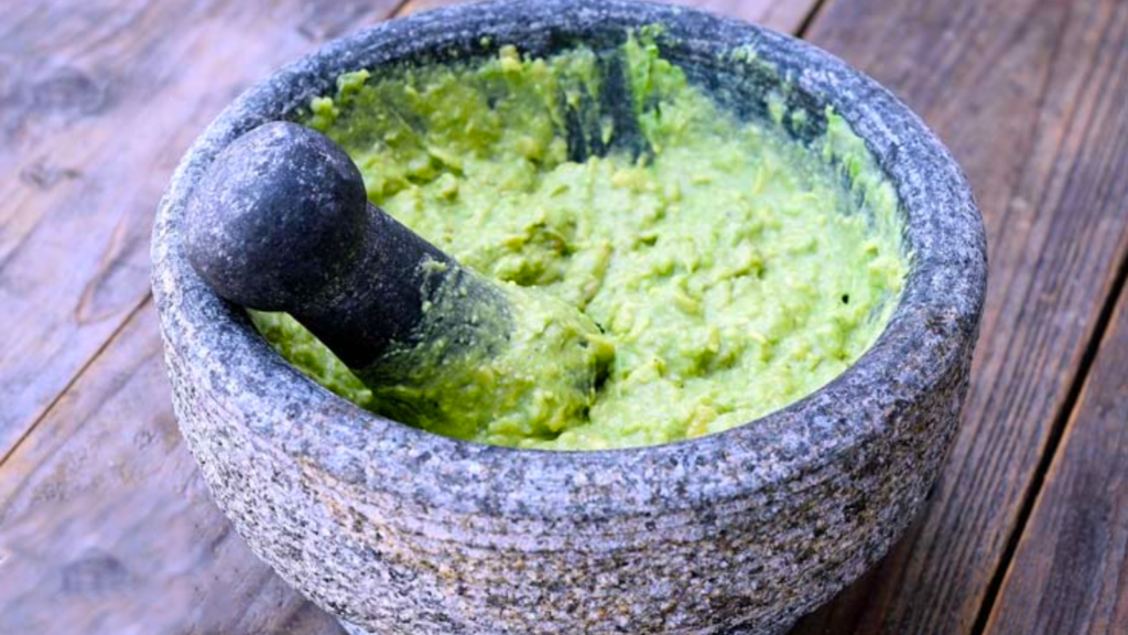 Guacamole in a mortar. The pestle stands in the guacamole.