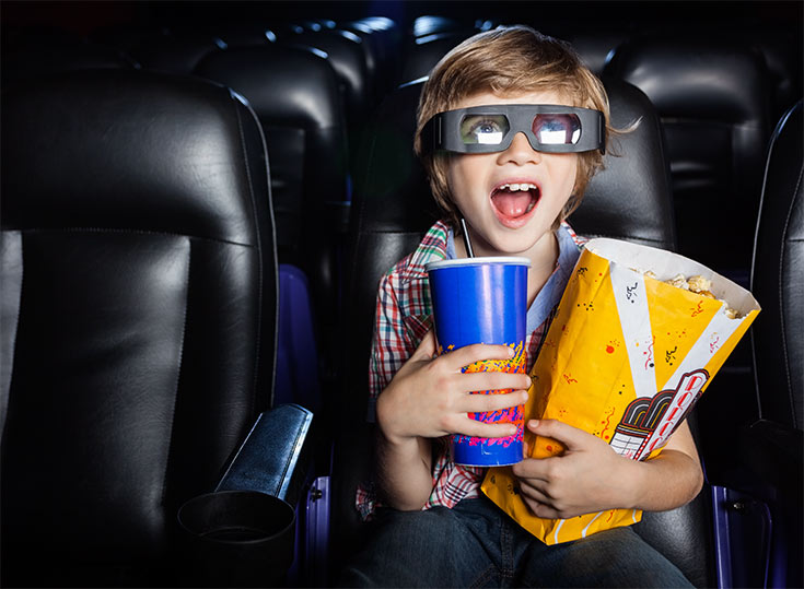 A young boy watching a movie holding a drink and a popcorn bag.