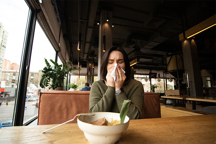 A woman blowing her nose at a restaurant table.