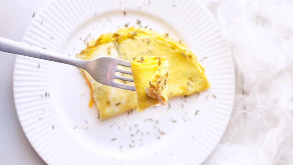 A fork lifts up a bite of a one egg omelet.