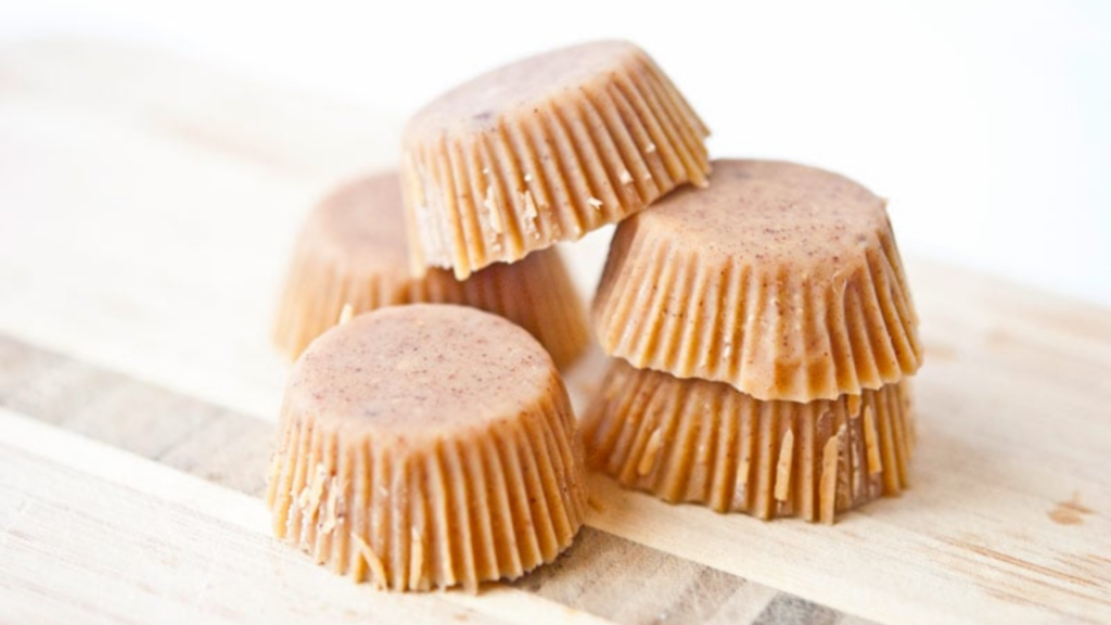 A pile of peanut butter fat bombs lay on a wood surface.