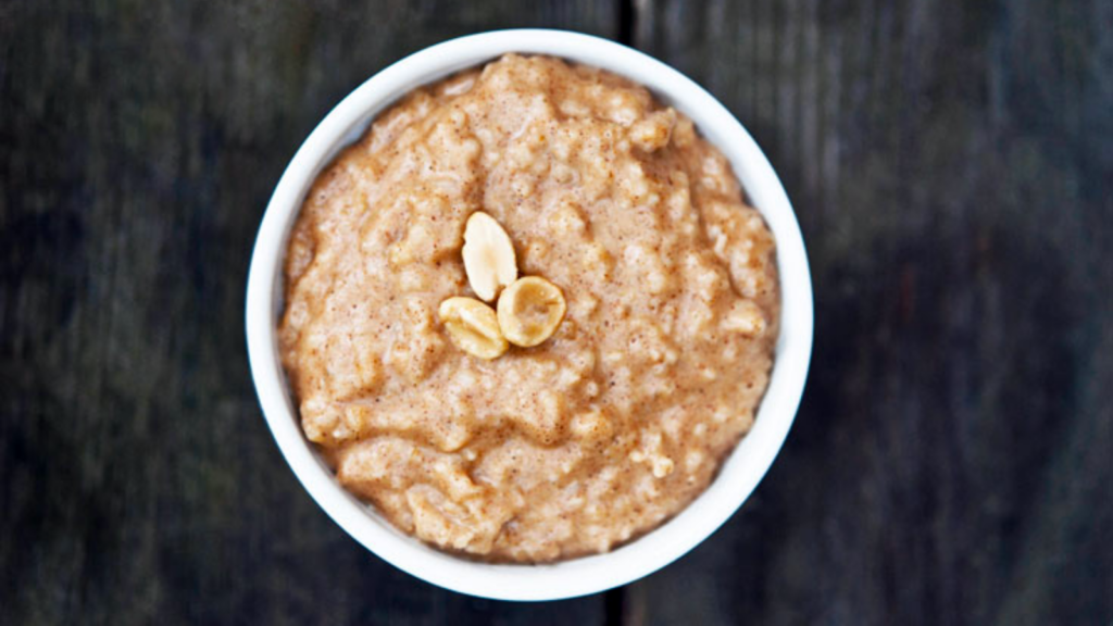 An overhead view of a white bowl full of peanut butter oatmeal and garnished with three peanuts.