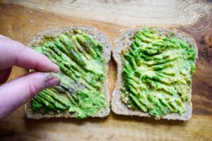 Sprinkling pepper over avocado smashed onto toast.