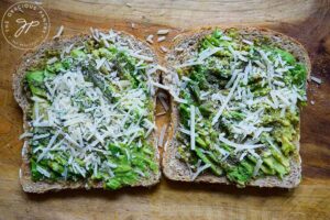 Two finished slices of Pesto Avocado Toast laying next to each other on a cutting board.