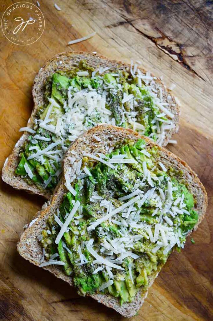 Two slices of Pesto Avocado Toast laying partial stacked on a wood cutting board.