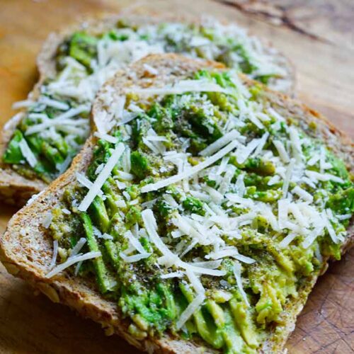 A front view of two slices of Pesto Avocado Toast laying on a cutting board, partially stacked.