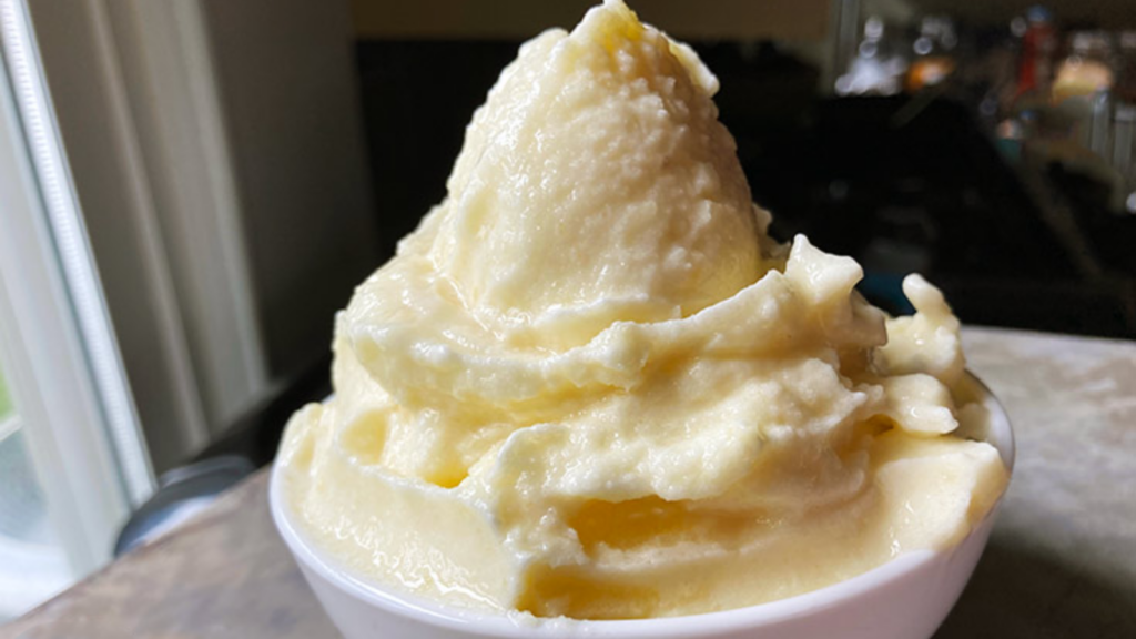 A white bowl on a table filled with a heap of pineapple whip.