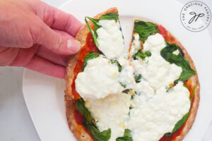 A hand reaches for a slice of Pita Pizza from a white plate.
