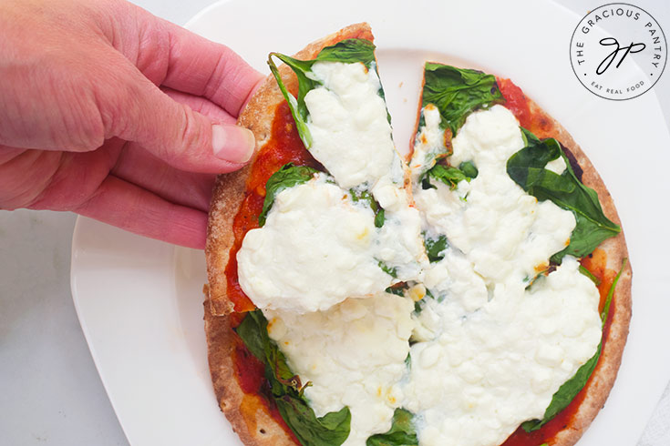 A hand reaches for a slice of Pita Pizza from a white plate.
