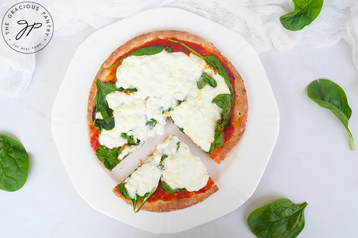 A slice of Pita Pizza sits removed from the rest of the pizza on a white plate.
