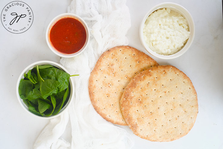 Pita Pizza Recipe ingredients on a white surface.