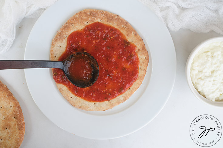 Topping the pita bread with pizza sauce.