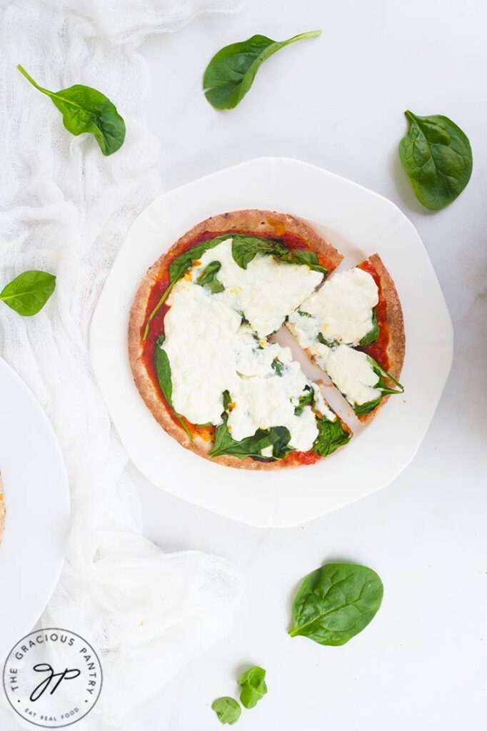 An overhead view of a slice of Pita Pizza pulled back from the rest of the pizza on a white plate.