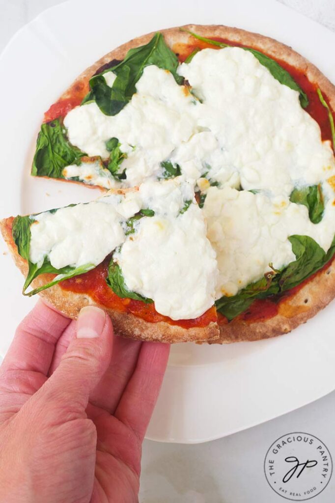 A hand holds a slice of Pita Pizza.