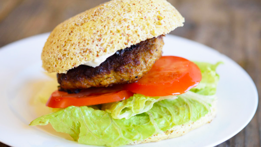 A single pork burger on a bun with tomato slices and lettuce.