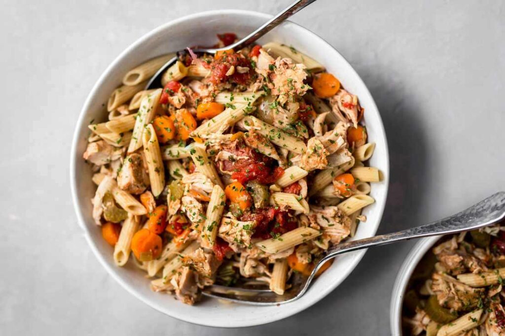 A white bowl filled with pork ragout. Serving spoons lay in the bowl.