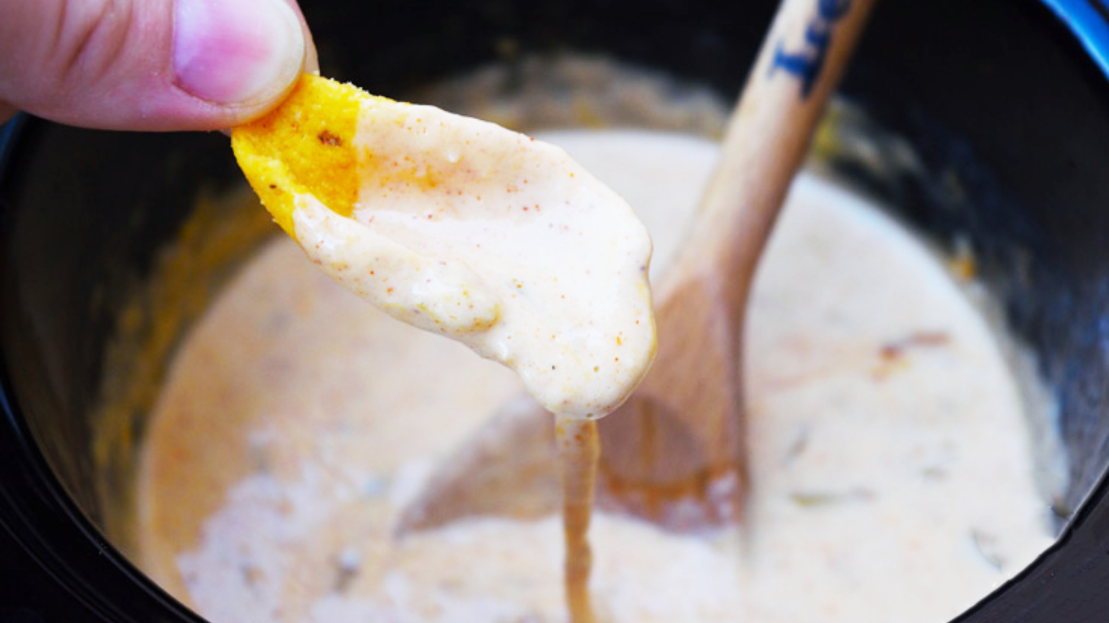 A chip being held over a pot of queso with queso dripping down off the chip.