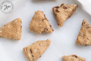 Unbaked Raisin Scones laying on a parchment-lined baking pan.