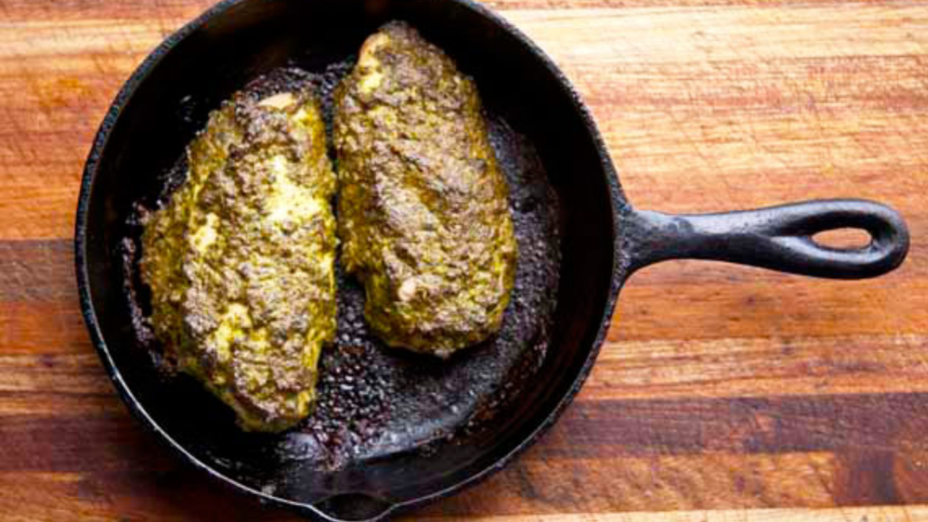 An overhead view of two pesto-covered chicken breasts in a cast iron skillet.