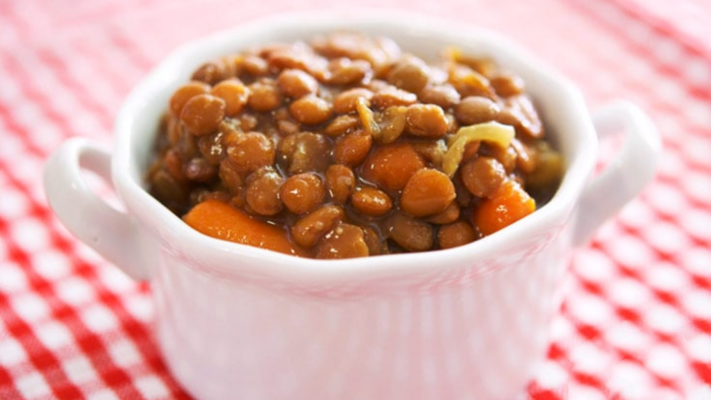 A small white crock on a red and white checkered tablecloth holds a serving of slow cooker lentil soup.