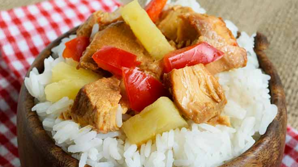 A wooden bowl holds rice topped with slow cooker Hawaiian Chicken