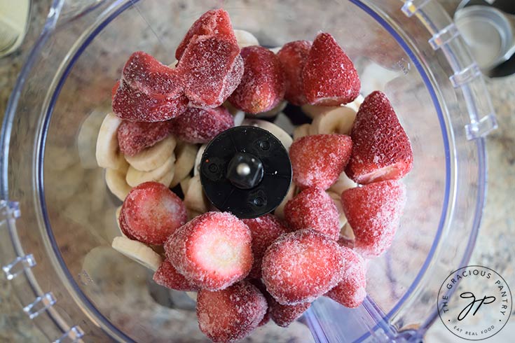 Frozen strawberries added to frozen banana slices in a food processor.
