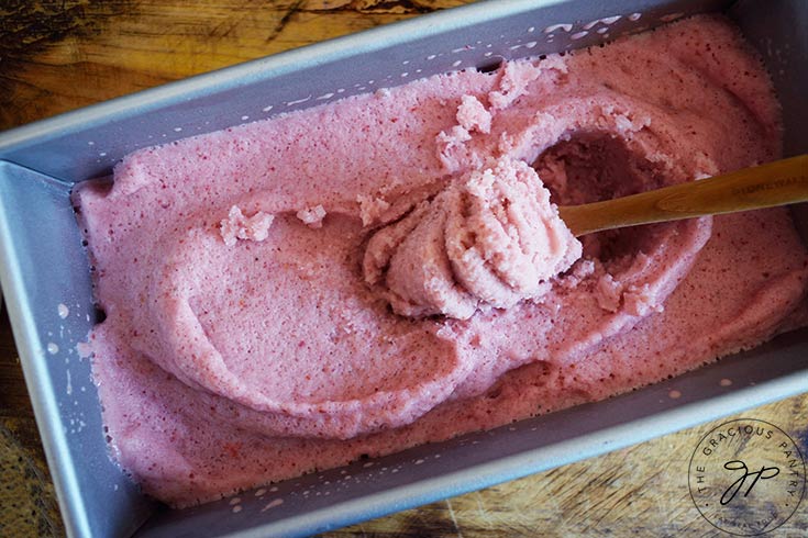 A wood spoon scoops out some frozen Strawberry N'ice Cream from a loaf pan.