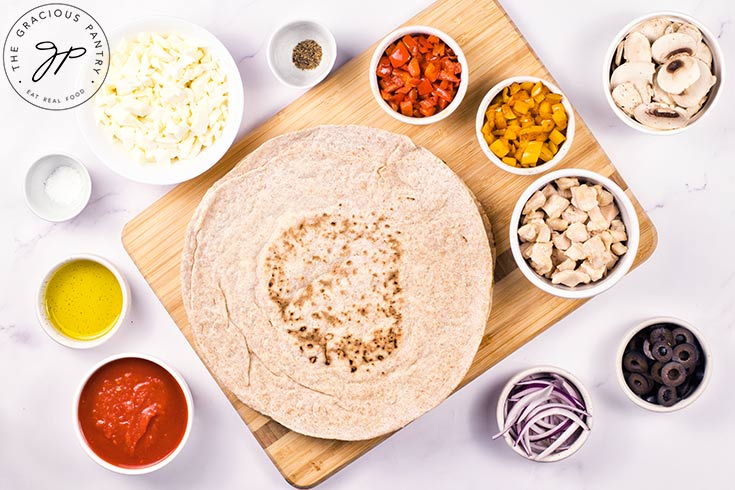 All the ingredients for a Supreme Pizza gathered in individual bowls around a cutting board.