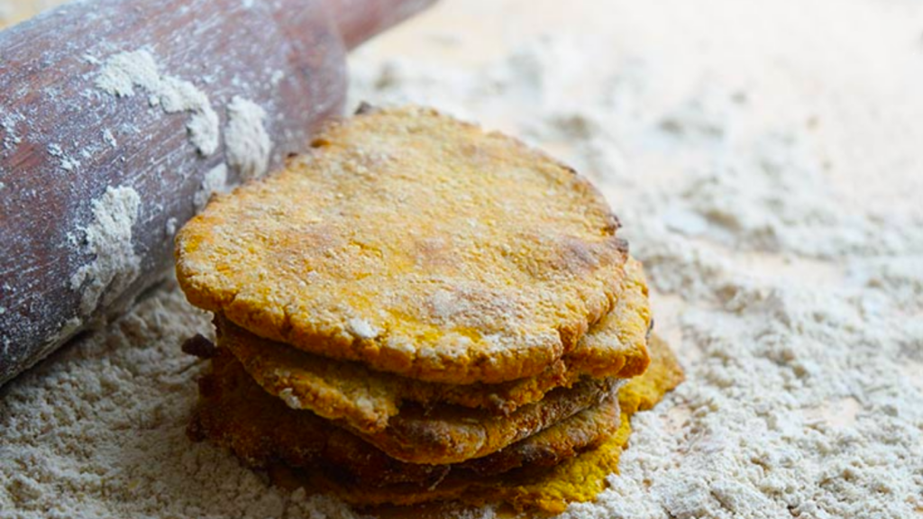 A stack of sweet potato flatbread sits next to a rolling pin on a floured surface.