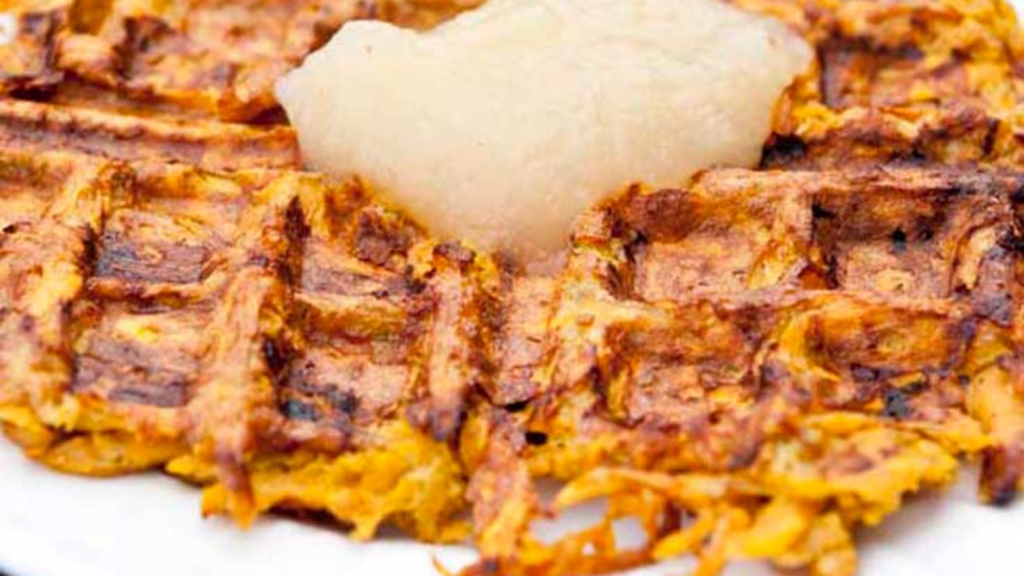 A closeup of a single sweet potato waffle with apple sauce on top.