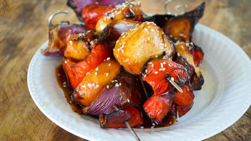 A white plate holds a few teriyaki chicken kabobs.