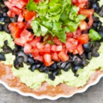 An overhead view of a white, fluted dish holding layers of tex mex dip.