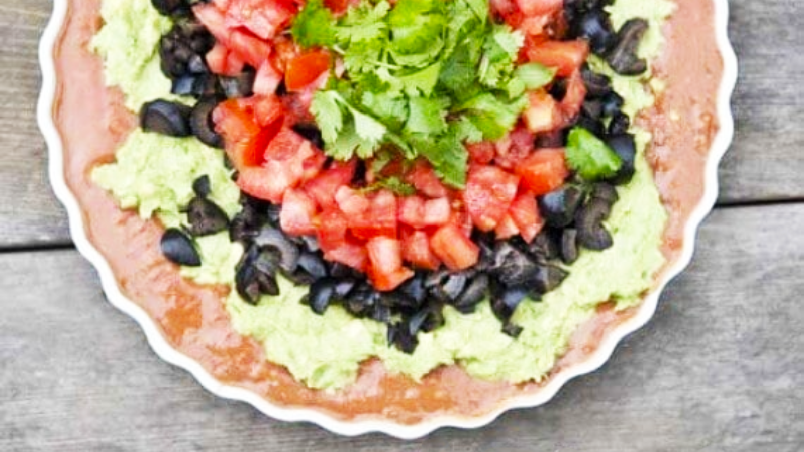 An overhead view of a white, fluted dish holding layers of tex mex dip.
