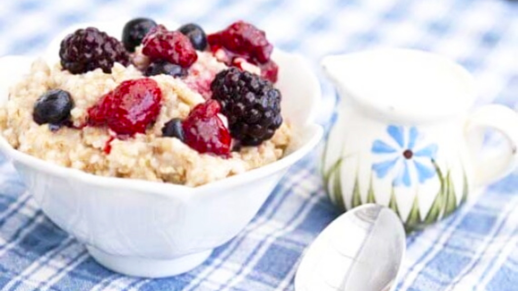 A white fluted bowl sits on a table and is filled with triple berry oatmeal.