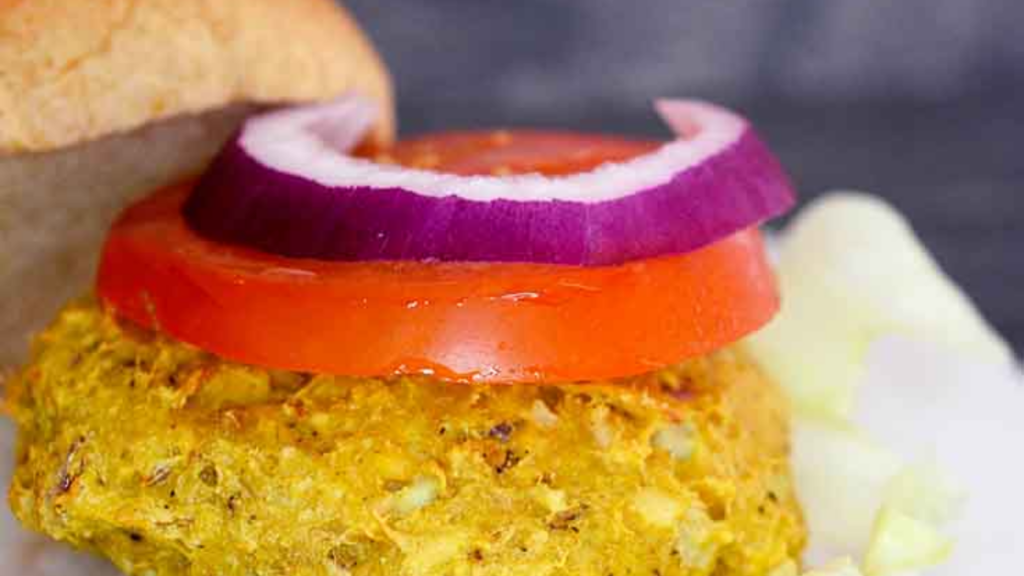 A closeup of a tuna burger with a tomato and onion slice on it.