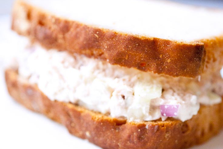 A close up of a tuna fish sandwich on a white background.