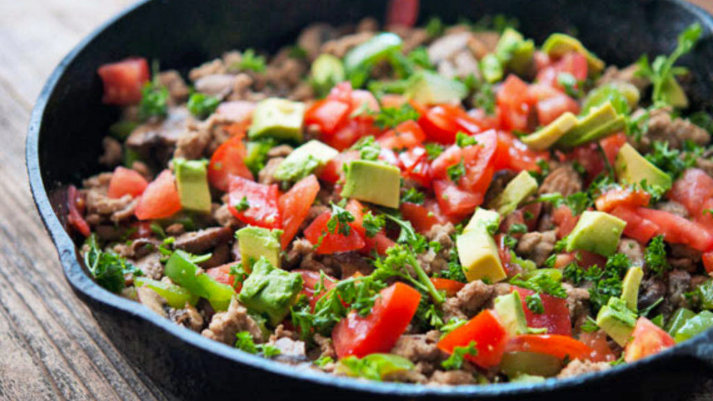 A cast iron skillet full of turkey vegetable skillet and garnished with fresh tomatoes and avocado.