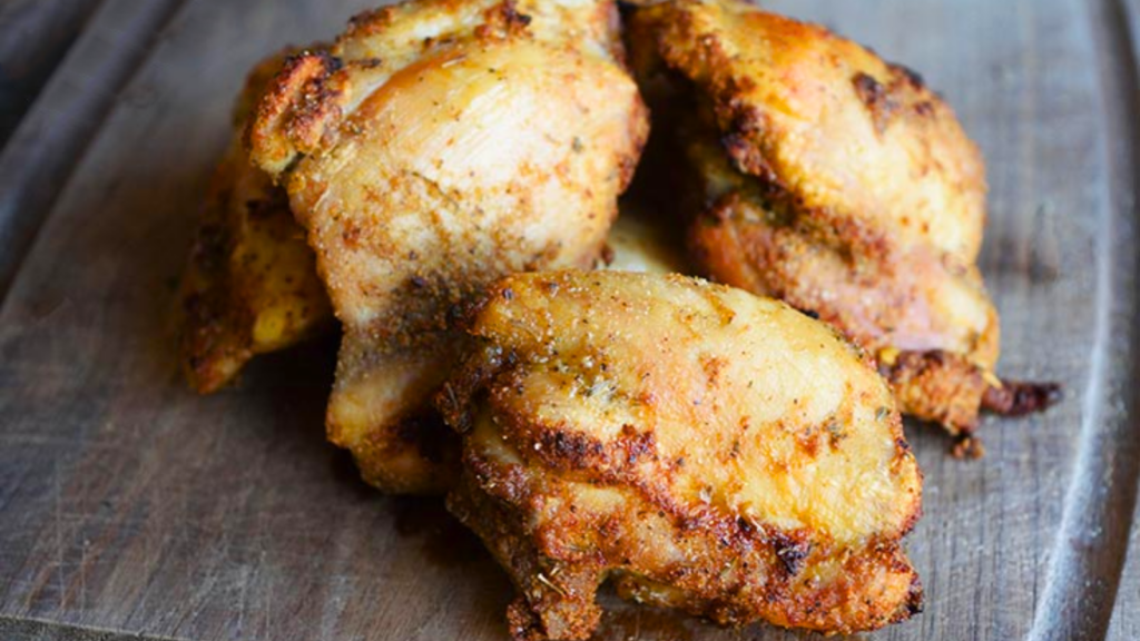 Three tuscan chicken thighs lay on a wood cutting board.