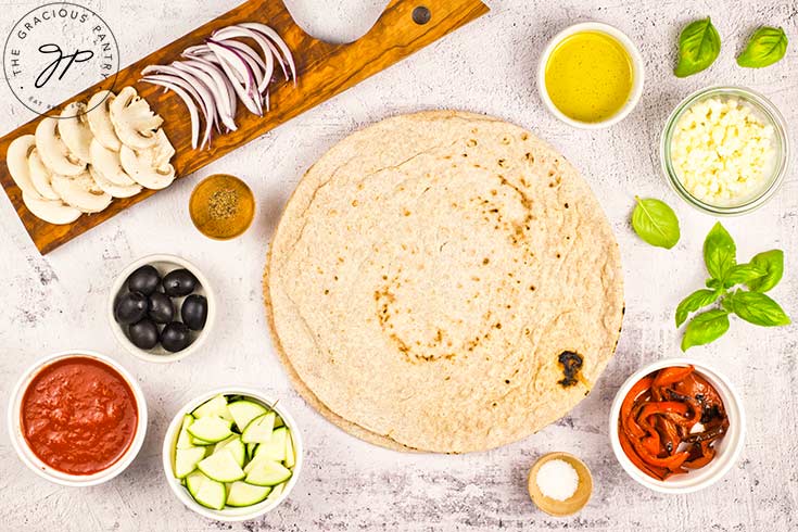 All ingredients for a Veggie Pizza gathered and prepped on a white surface.