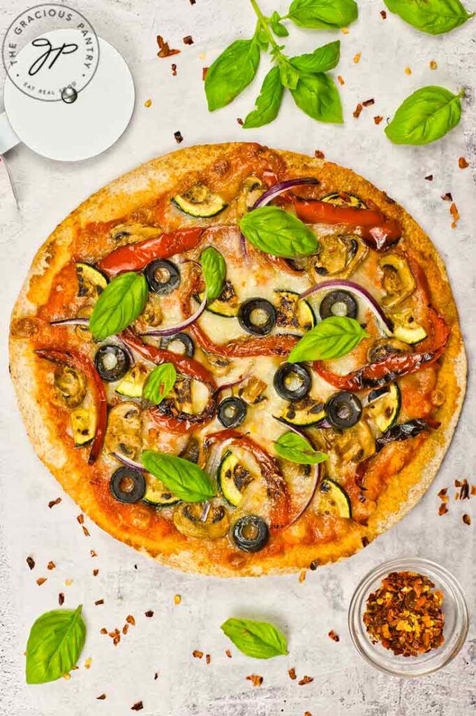 Fresh basil leaves sprinkled over a cooked veggie pizza.