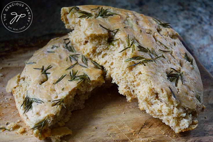 A finished loaf of Whole Wheat Focaccia Bread, broken in half an laying on a cutting board.