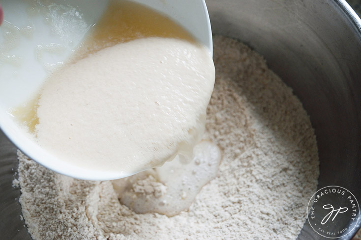 Adding a foamy yeast mixture to a flour mixture in a large mixing bowl.