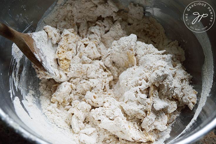 Partially mixed Whole Wheat Focaccia Bread dough in a mixing bowl with a wooden spoon.