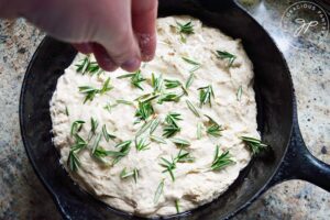 Sprinkling the top of the unbaked focaccia bread with additional salt.