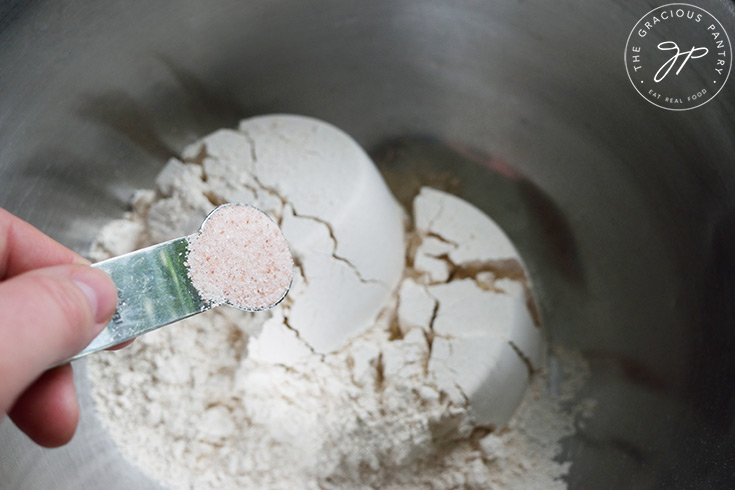 Adding salt to flour in a mixing bowl.