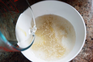 Adding warm water to a medium mixing bowl of honey and yeast.