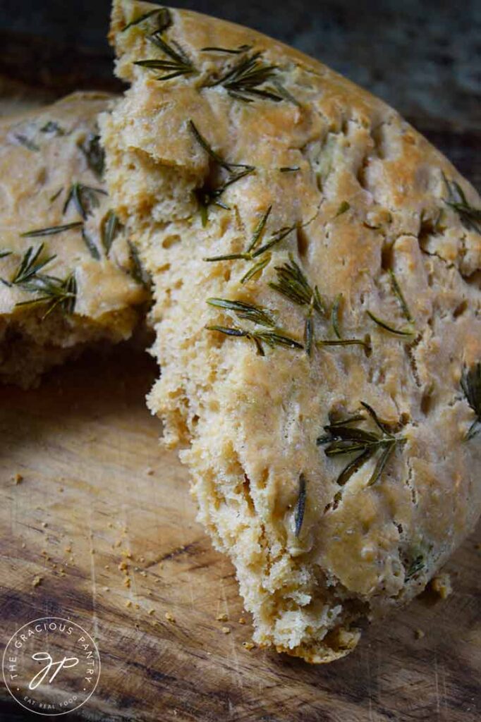 A round Whole Wheat Focaccia Bread torn in half on a cutting board.