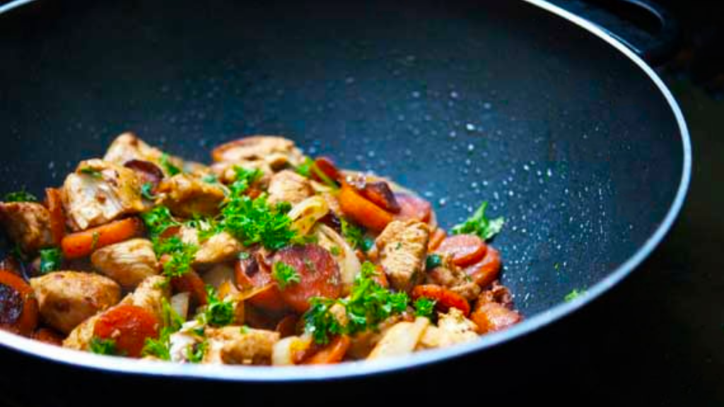 A black wok holds wok-style garlic chicken and carrots garnished with parsley.