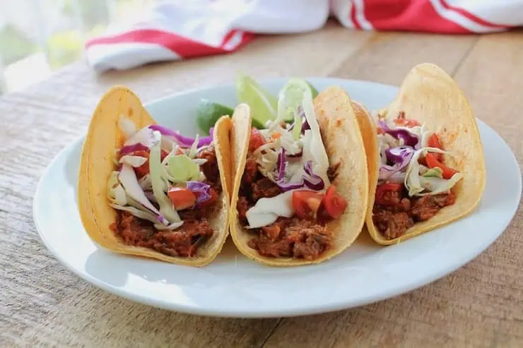 Three tacos lined up on a white plate.