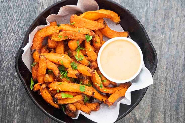 An overhead view of a cast iron skillet filled with sweet potato fries and a small dish of dip.